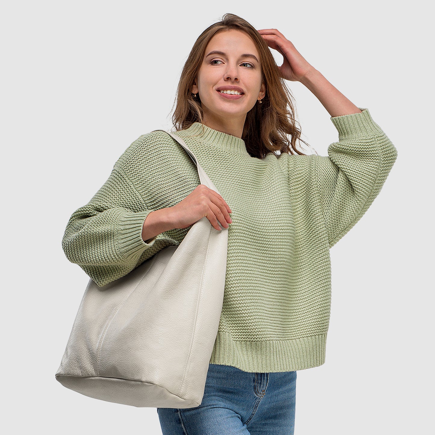 Woman in a green sweater smiles while holding a large white bag, enhancing her casual look.
