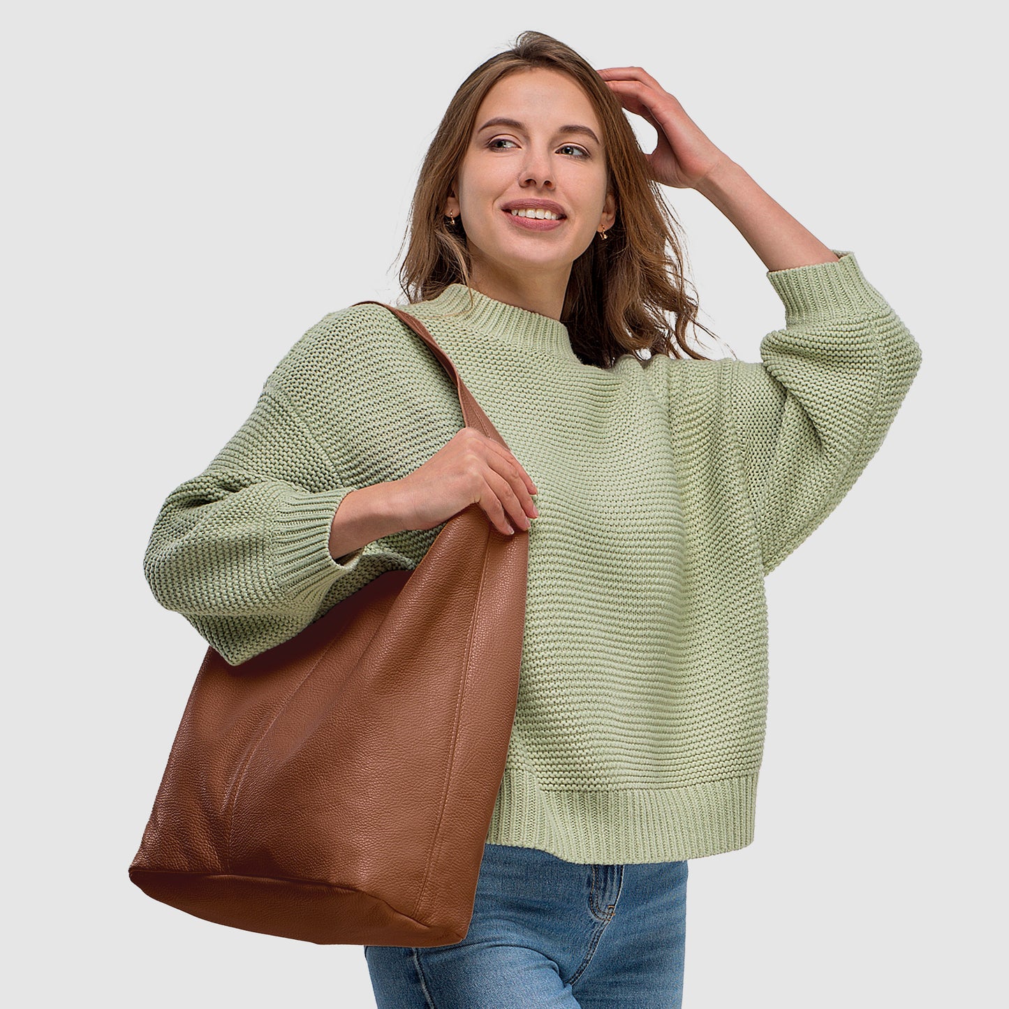 Woman in a light green sweater holds a brown handbag, smiling against a neutral background.