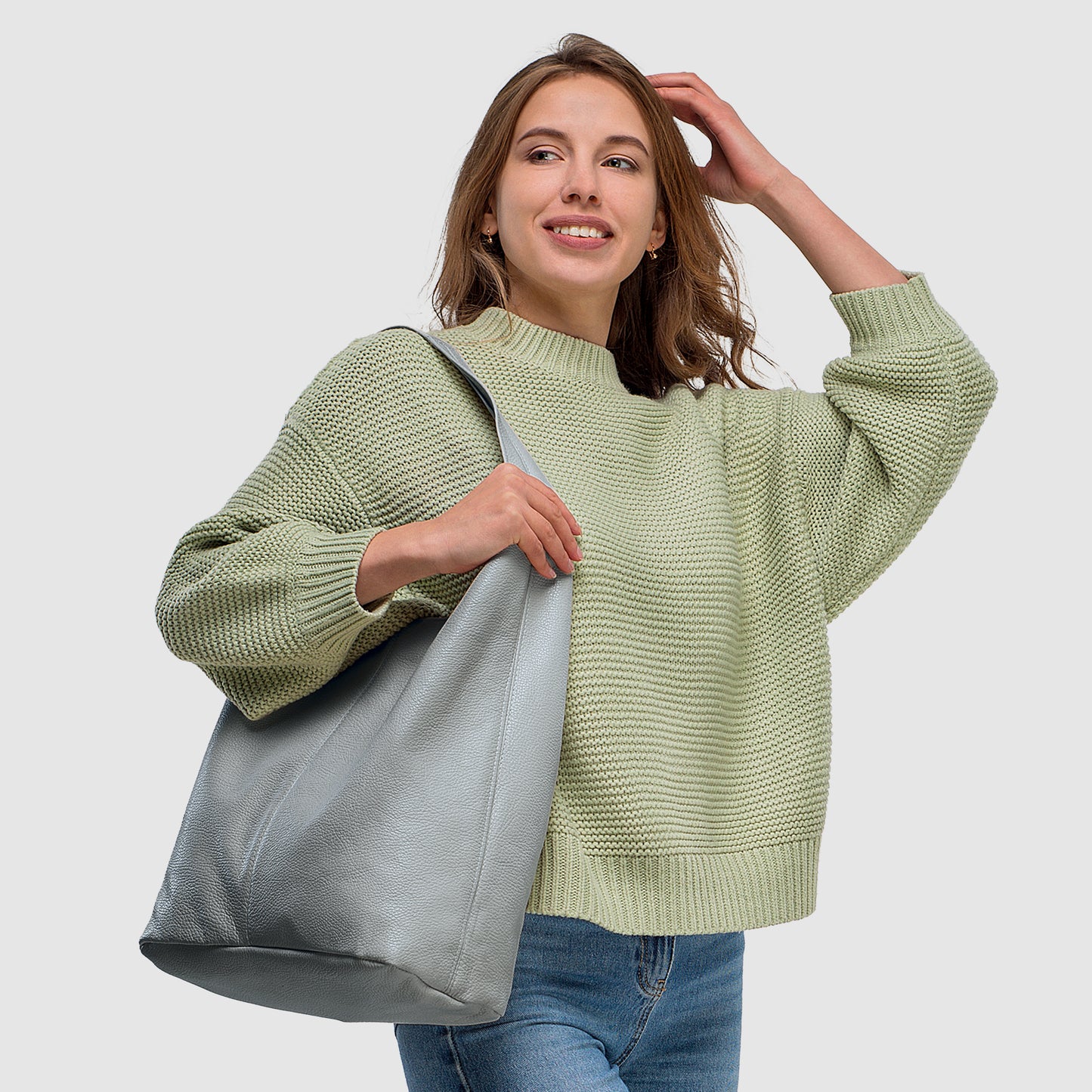 Woman in a light green sweater smiles while holding a gray tote bag against a neutral background.