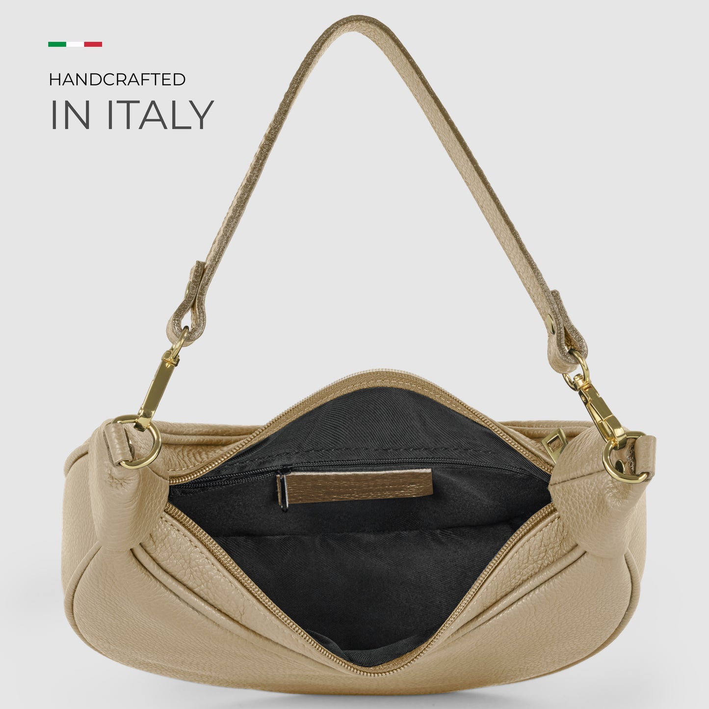 A crescent-shaped handbag in beige Italian calf leather with a short strap is shown open, revealing a black fabric-lined interior and a small inner pocket. Text on the left reads Handcrafted in Italy with a small Italian flag above it.