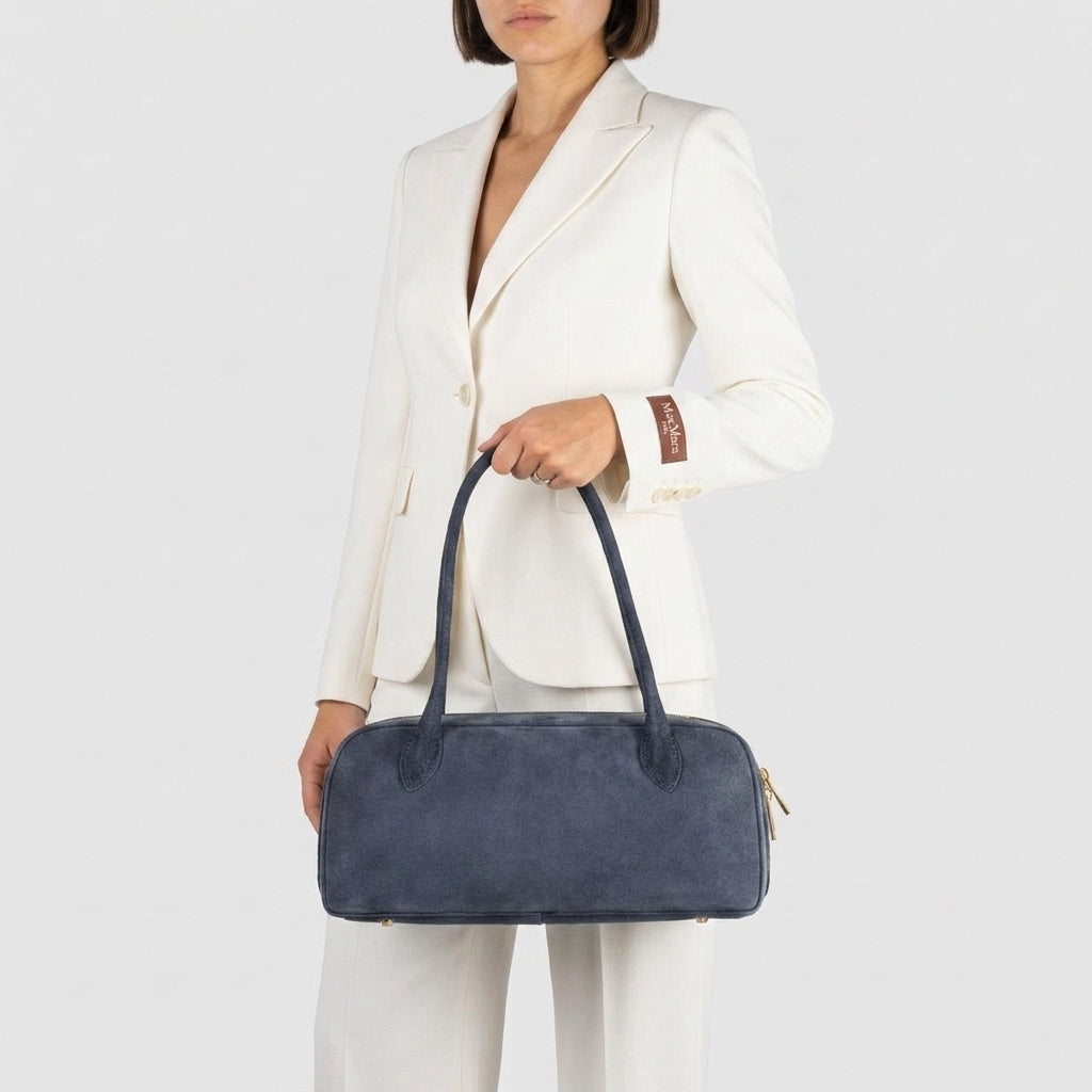 A woman in a white suit holds a large Italian suede purse with two top handles, standing against a plain light gray background.