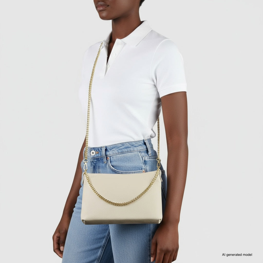 A woman wearing a white polo shirt and blue jeans carries a small structured handbag with a gold chain shoulder bag strap over her shoulder, standing against a plain light background.