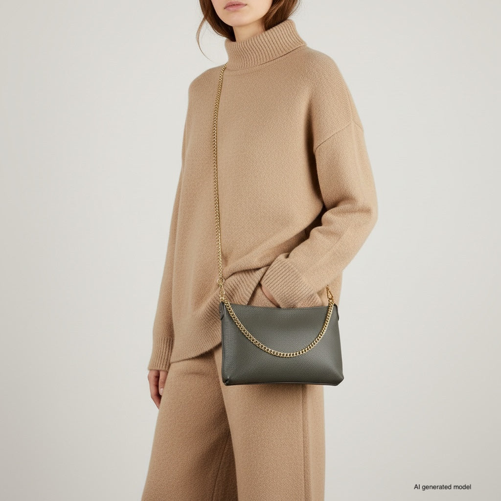A woman in a beige turtleneck sweater and matching pants poses with an Italian leather crossbody purse featuring a gold chain strap. Her hand is in her pocket, and her face is partially out of frame.