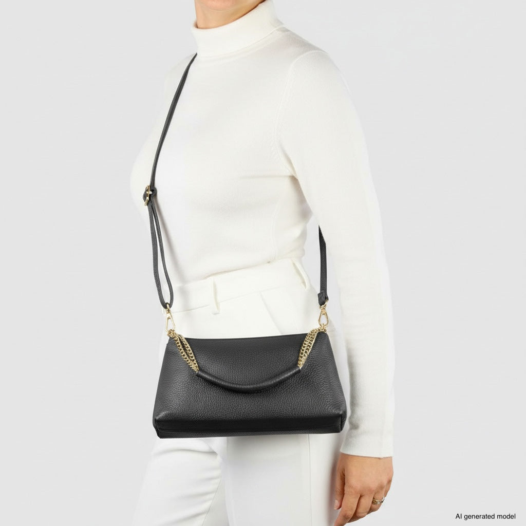 A person wearing a white turtleneck and white pants carries a genuine leather crossbody handbag with gold hardware, standing against a plain light background.
