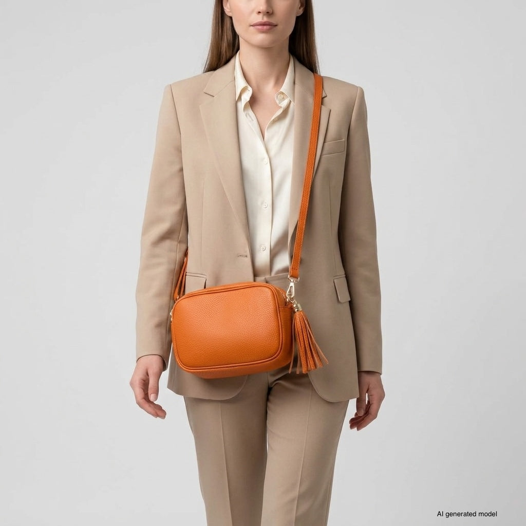 A woman in a beige suit and white blouse carries an Italian leather crossbody bag with a tassel, standing against a plain light gray background.