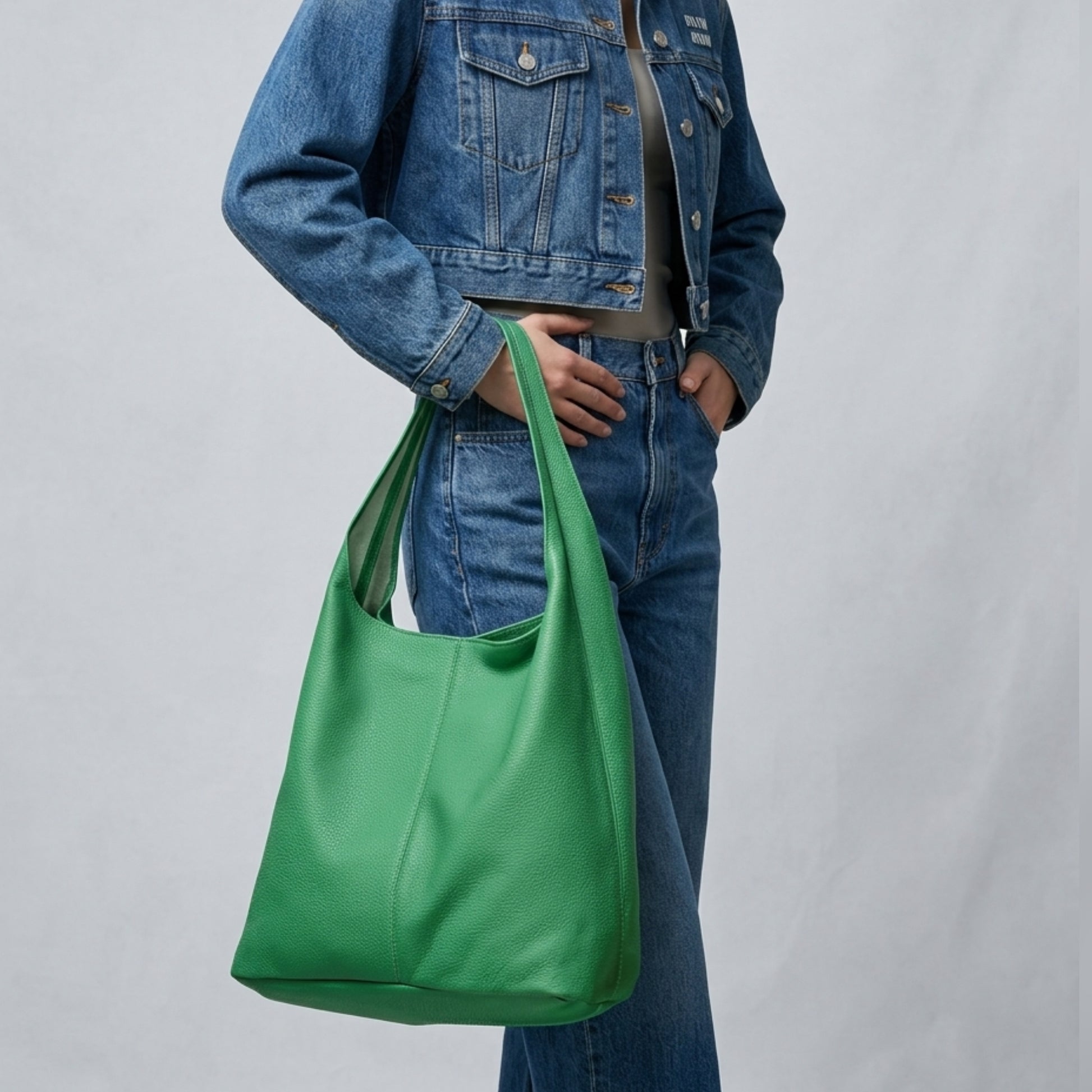 A person wearing a blue denim jacket and jeans holds a large Italian hobo bag crafted from genuine calf leather against a plain light gray background.