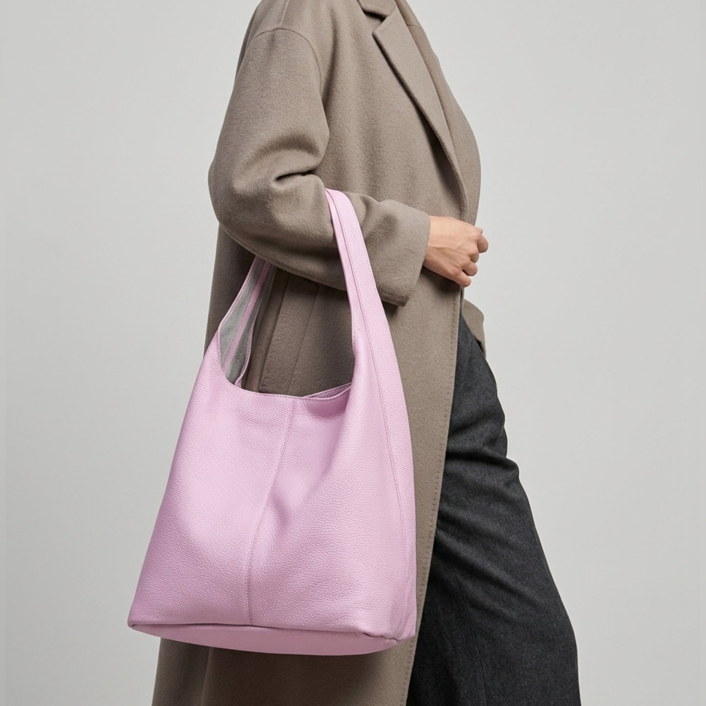 A person wearing a taupe coat and dark pants carries a large, soft pink Italian hobo bag crafted from genuine calf leather over their shoulder against a plain light background.