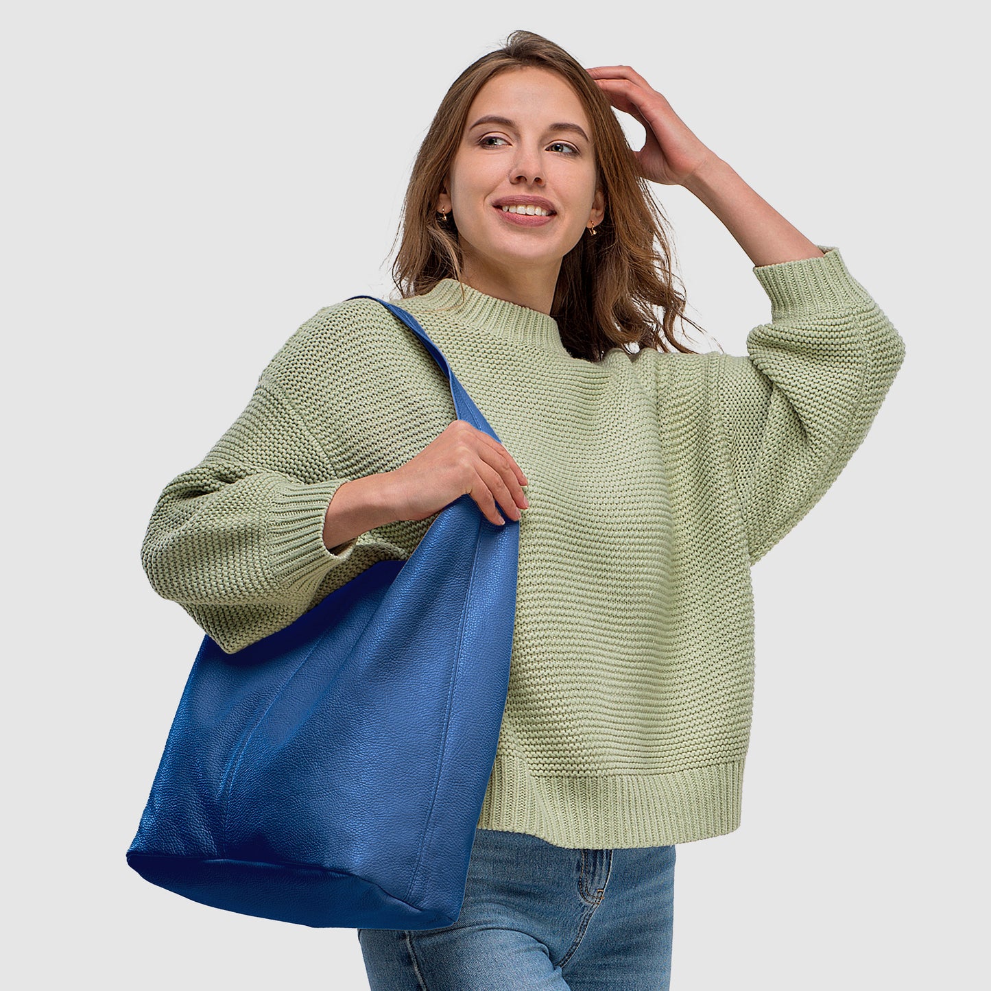 Woman in a light green sweater smiles while holding a blue tote bag, set against a neutral background.