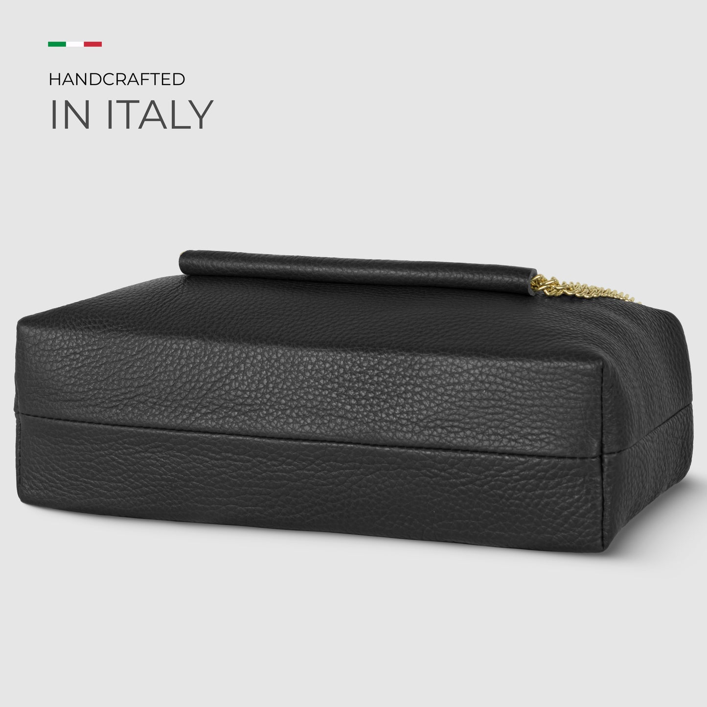 A rectangular black Italian leather bag with a gold chain and handle, displayed on a light background. Text reads Handcrafted in Italy with a small Italian flag above. An elegant shoulder bag perfect for any occasion.