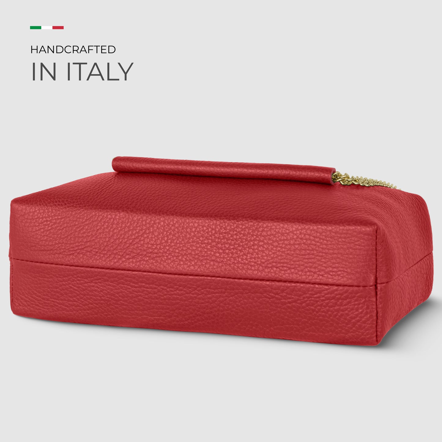 Rectangular red Italian leather bag with a gold chain handle resting on top, set against a light gray background. Text on the left reads Handcrafted in Italy with a small Italian flag above.