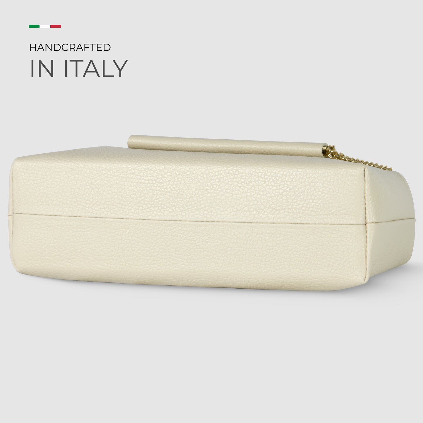 A rectangular, ivory-colored Italian leather bag with a gold chain, displayed on its side. Text reads Handcrafted in Italy next to a small Italian flag.