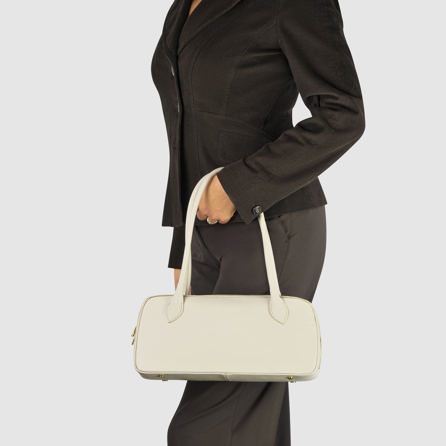 A person in a black blazer and pants is holding an Italian leather bag with long handles, against a plain light background. The person’s face is not visible.