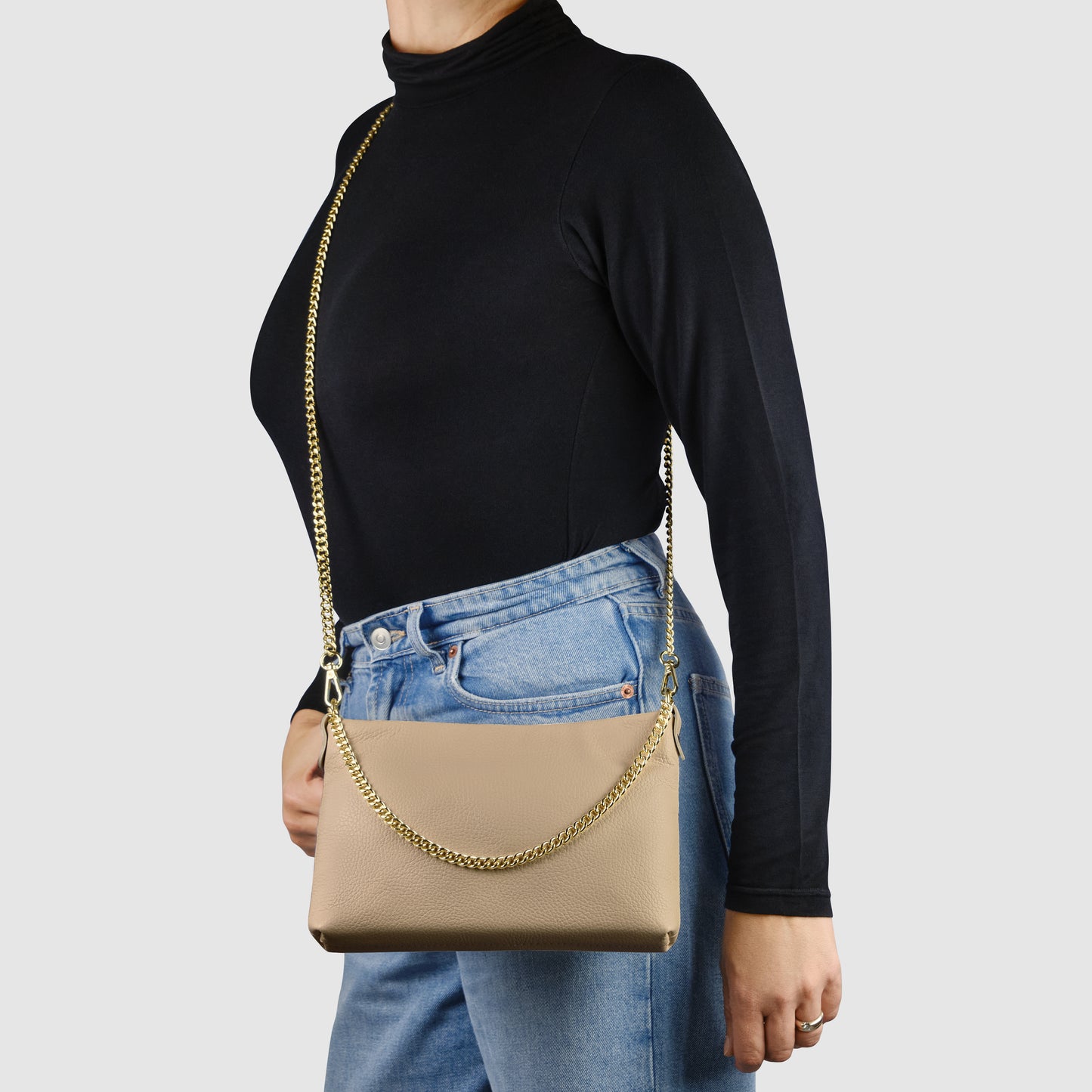 A person wearing a black long-sleeve top and blue jeans is carrying an Italian leather crossbody purse with a gold chain strap over their shoulder. The background is plain and light-colored.