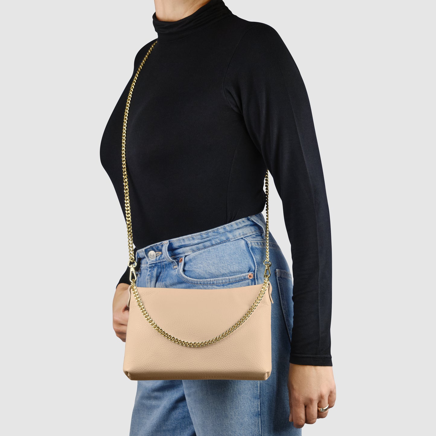 A person wearing a black long-sleeve top and blue jeans stands sideways, carrying an Italian leather crossbody purse with a gold chain strap over their shoulder. The background is plain light gray.