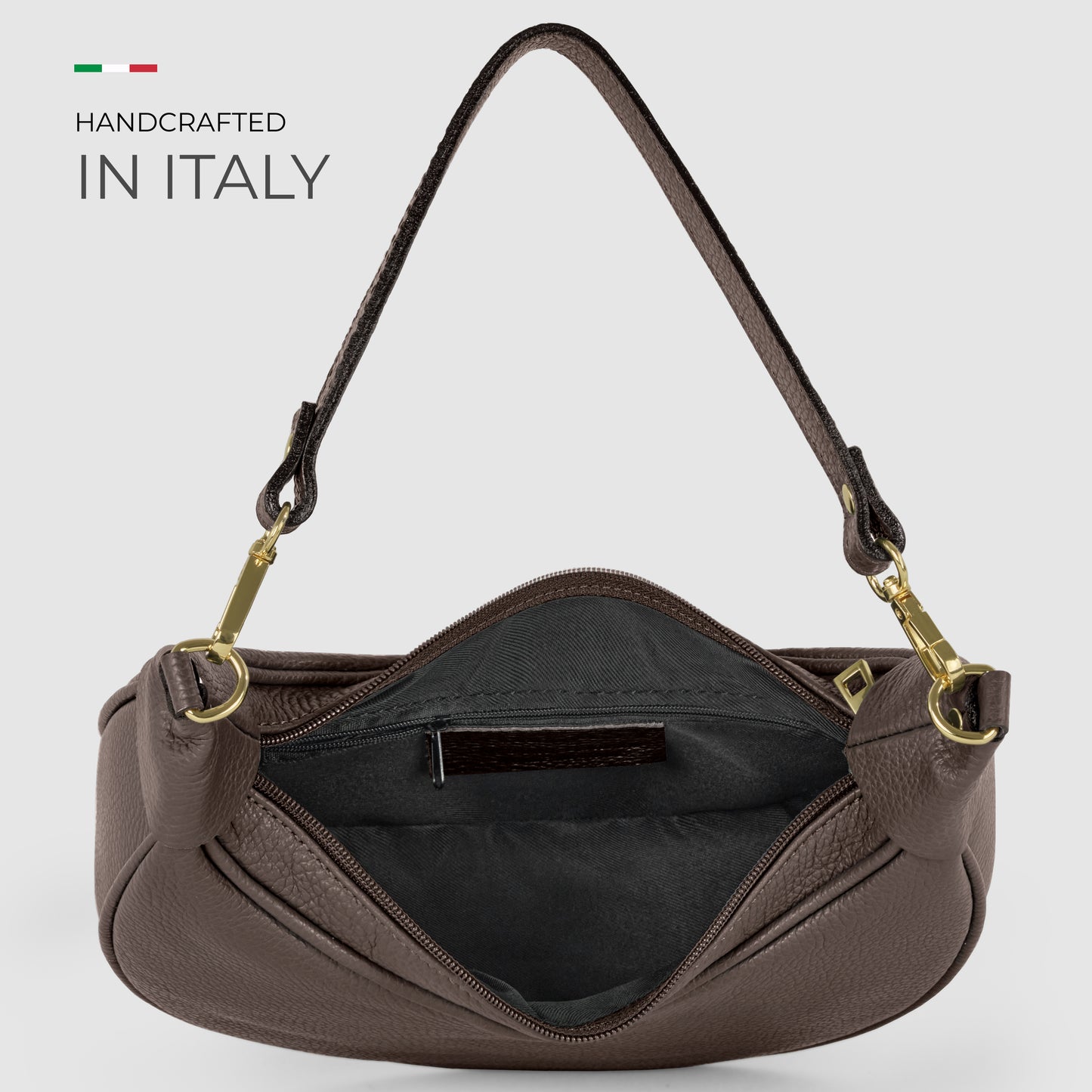 A crescent-shaped handbag in brown Italian calf leather with gold hardware is shown open to display its black fabric interior and inner pocket. Text reads Handcrafted in Italy with a small Italian flag above it.