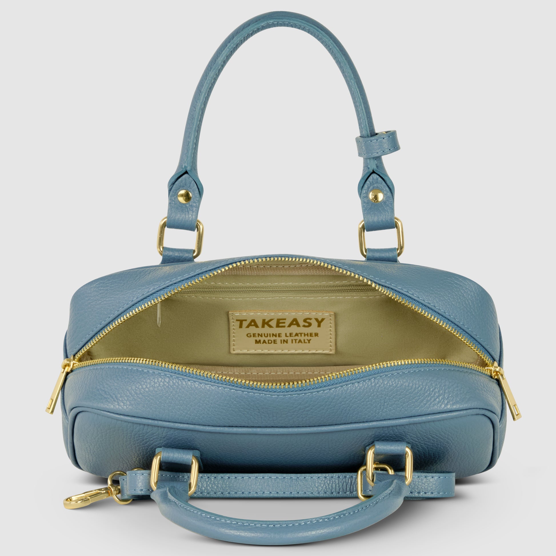 A blue Italian leather handbag with gold hardware, unzipped to reveal a beige interior and a label that reads “TAKEASY Genuine Leather Made in Italy.” Two handles and a detachable strap complete this minimalist handbag.