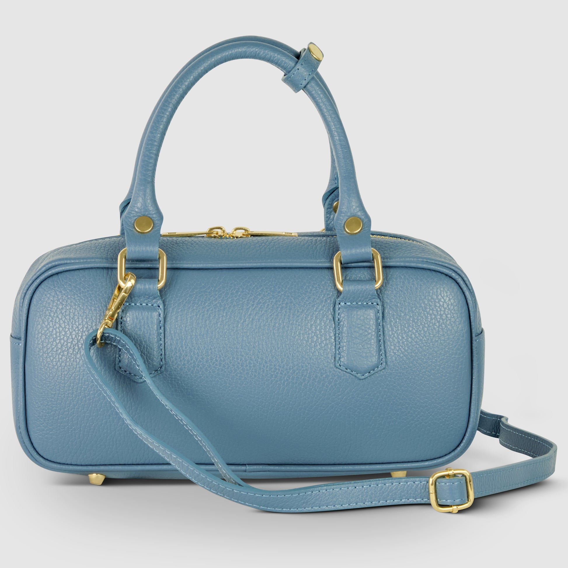 A small, structured pebbled leather bag in blue with two handles, a detachable shoulder strap, gold hardware, and a zip closure. This minimalist handbag features gold feet and a refined silhouette for everyday elegance.