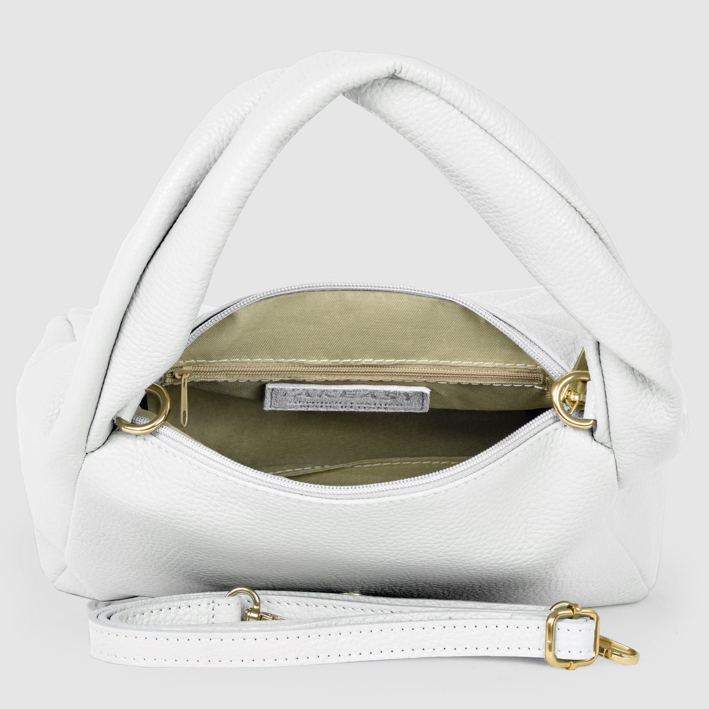 A minimalist handbag, handmade in Italy, featuring white leather with twisted handles, gold hardware, and a detachable strap. The open bag reveals a beige interior lining and a zippered pocket inside.
