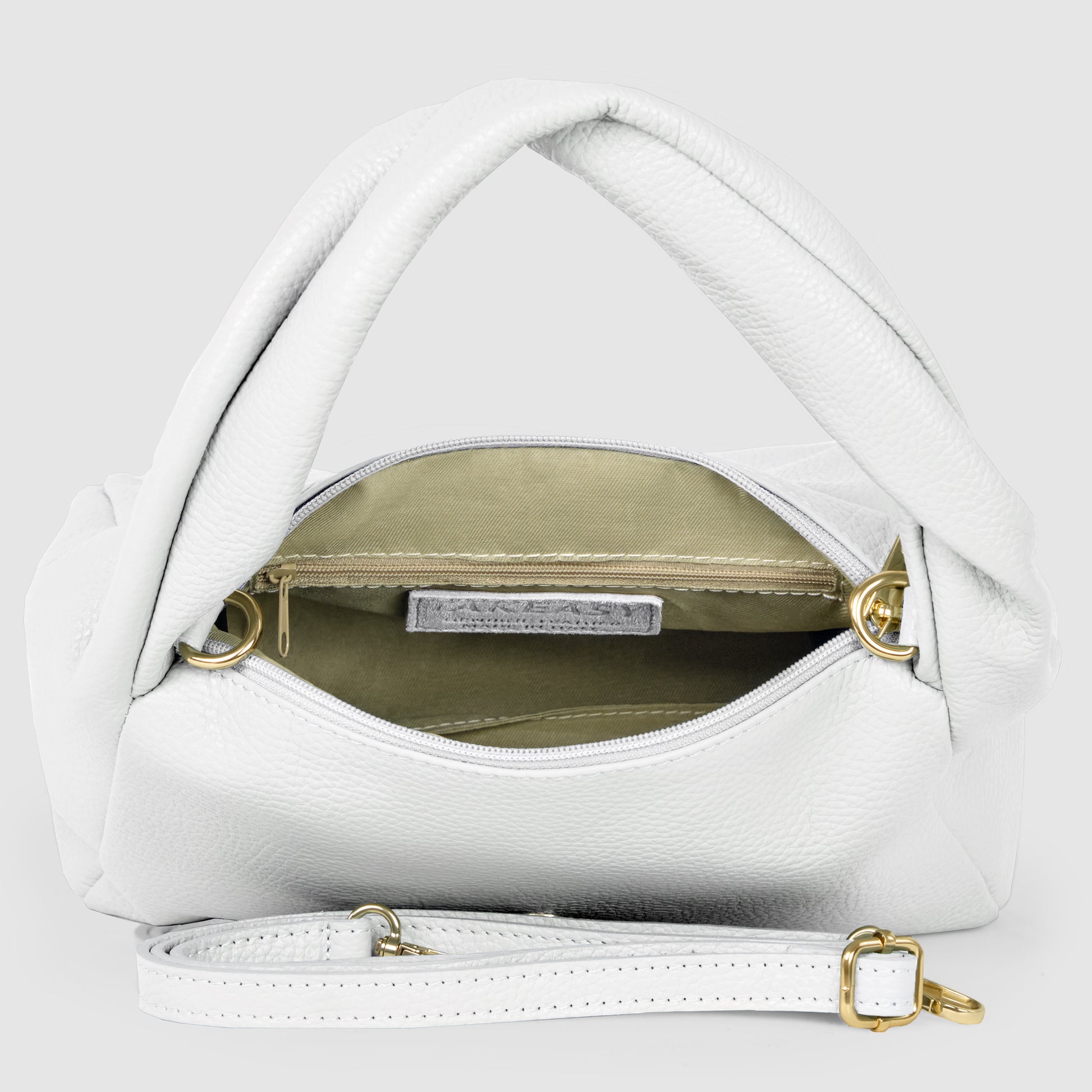 A minimalist handbag, handmade in Italy, featuring white leather with twisted handles, gold hardware, and a detachable strap. The open bag reveals a beige interior lining and a zippered pocket inside.