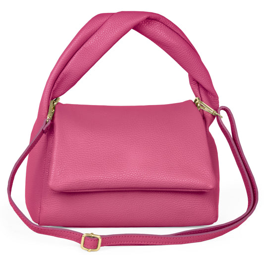 A pink minimalist handbag, handmade in Italy from fine leather, features a folded top handle, gold-tone hardware, and a matching adjustable shoulder strap, displayed on a white background.