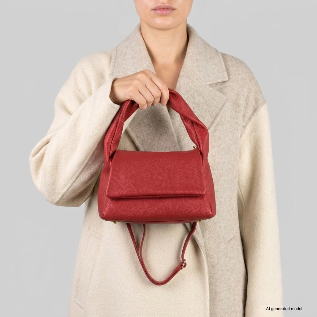 A person wearing a beige coat holds a medium rectangular handbag made of genuine calf leather by its top handle, with the bag’s shoulder strap hanging down. The background is plain gray.