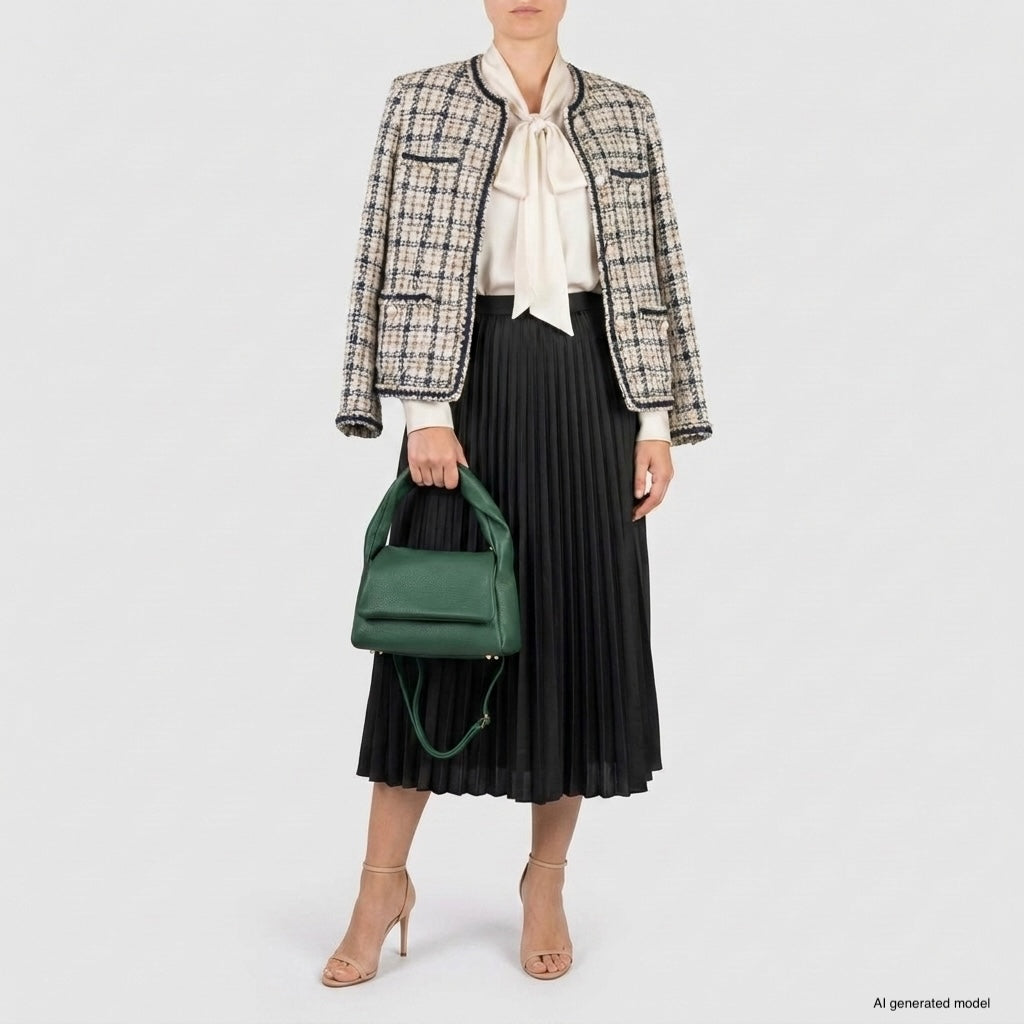 A woman in a tweed jacket, cream blouse with a bow, black pleated midi skirt, and nude heels holds a medium rectangular handbag made in Italy from genuine calf leather. The background is plain white. Her face is not visible.