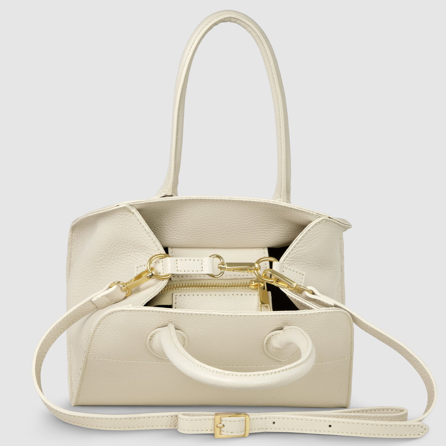 A cream-colored Italian leather handbag with gold hardware, double handles, an adjustable shoulder strap, and an open top revealing a small matching wallet inside. This elegant women’s handbag is set against a plain light gray background.