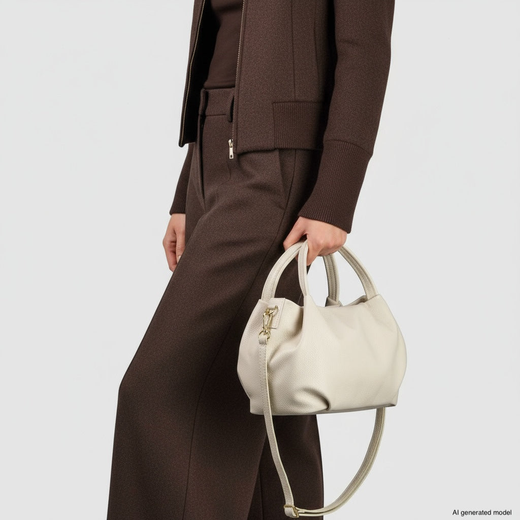 A person wearing a brown suit holds a large, white Italian leather handbag with both short and long handles against a plain white background.