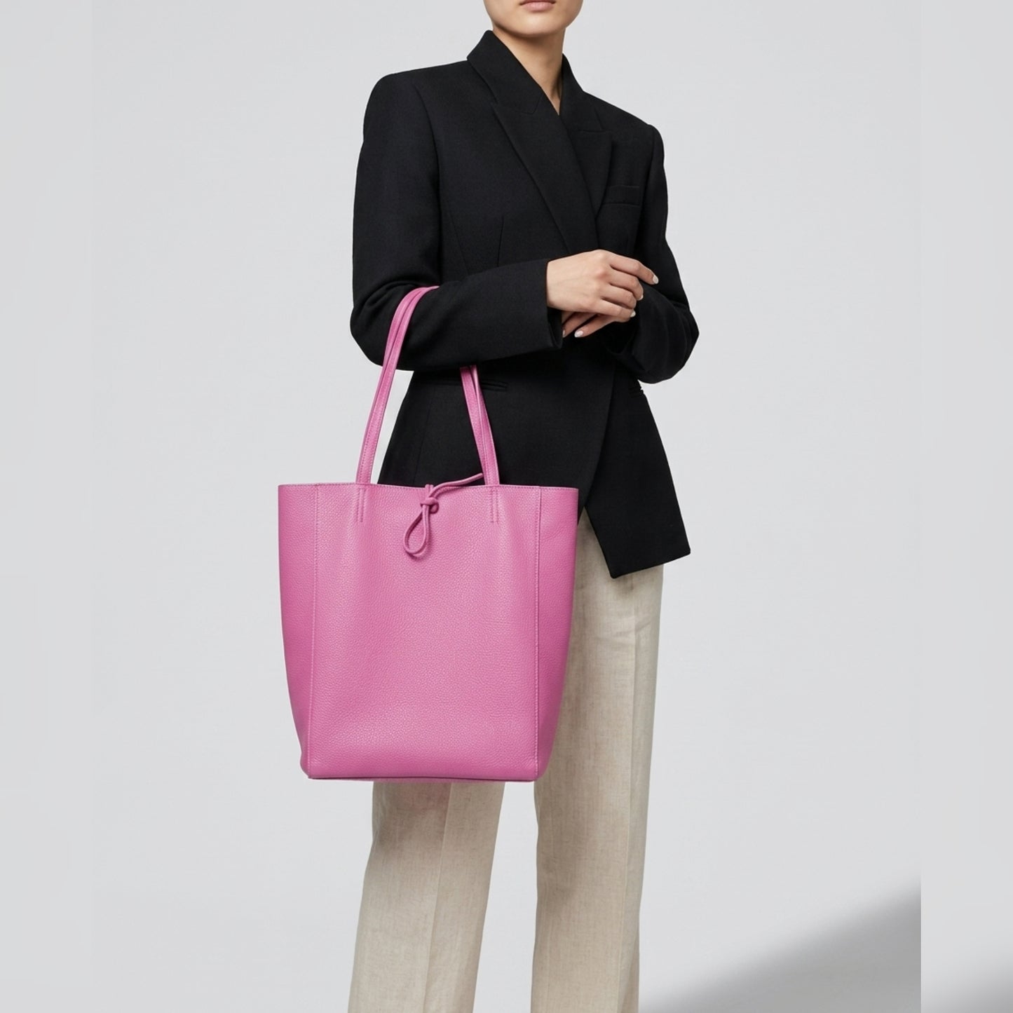 A person wearing a black blazer and beige pants holds a large Italian leather tote over their shoulder against a plain, light background.