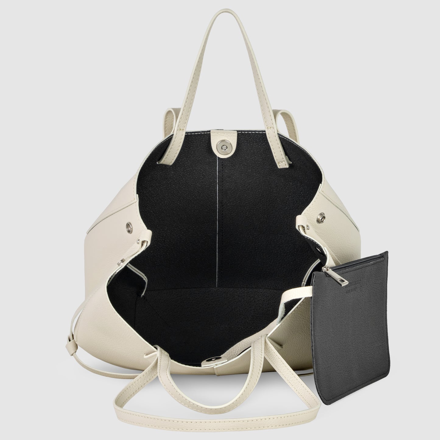 An open cream-colored convertible tote with black interior, handcrafted in Italy from Italian leather. It features a small detachable black zippered pouch on an inner strap, two handles, and a snap closure at the top.
