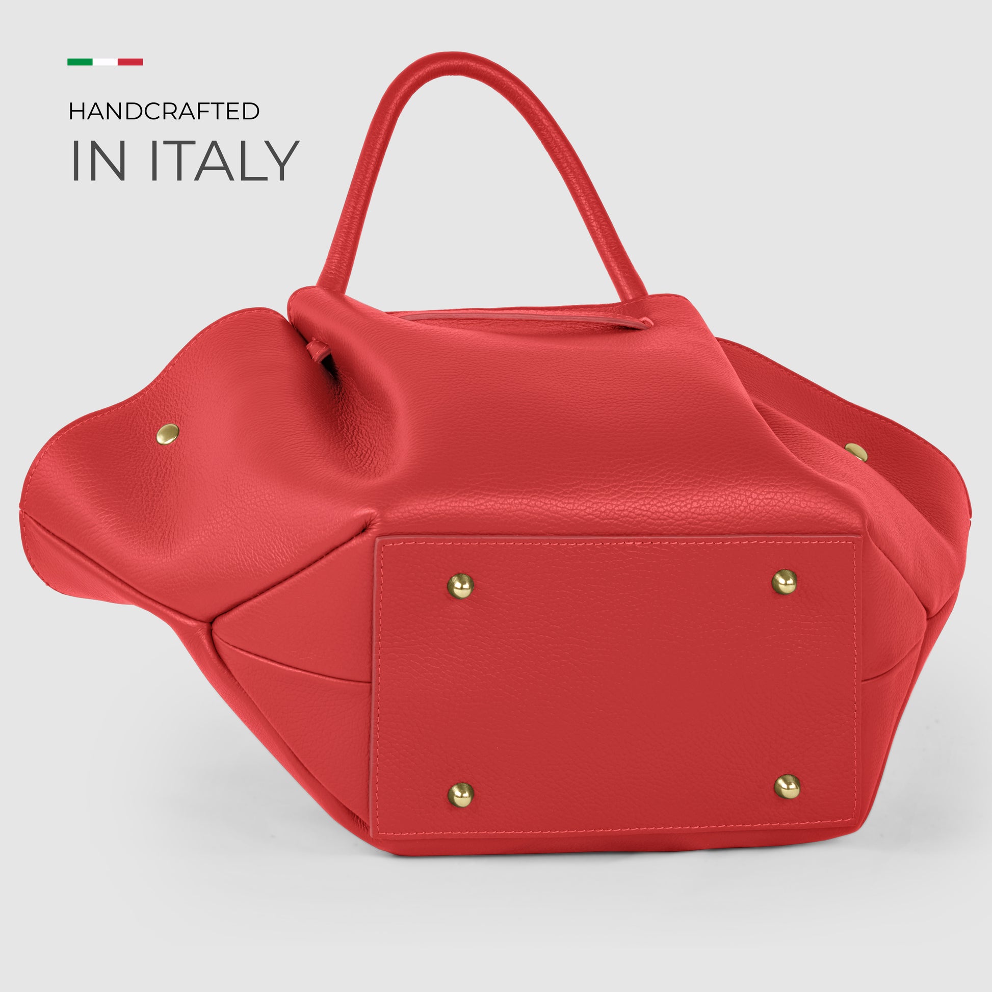 A red Italian leather bag with gold studs on the bottom is displayed against a light background. Text in the top left corner reads Handcrafted in Italy with a small Italian flag above it, highlighting Florentine craftsmanship.