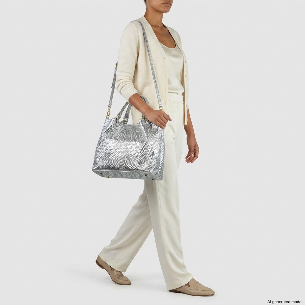 A person wearing cream-colored pants, a matching top, and cardigan carries a striking Italian suede handbag over their shoulder. They are also wearing tan loafers. The background is plain white.