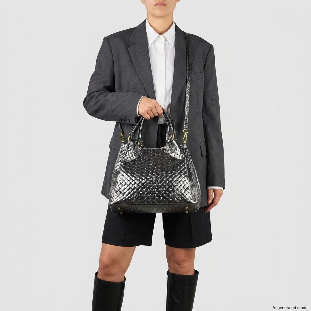 Person wearing a gray blazer, white shirt, black shorts, and knee-high boots holds a shiny, silver woven-effect handbag with both shoulder and top handles—showcasing authentic Italian craftsmanship—against a plain light background.