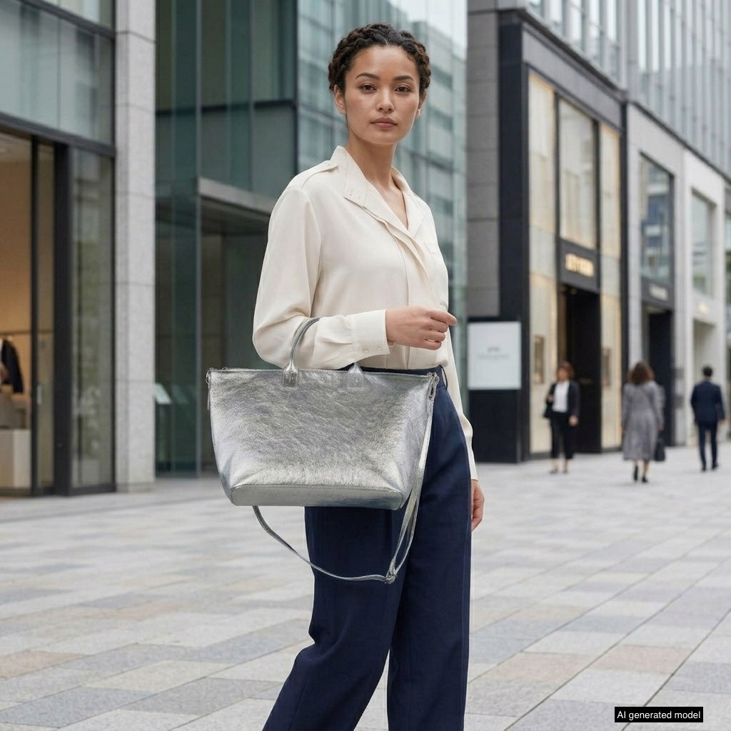 A woman stands on a modern city sidewalk wearing a cream blouse and navy pants, holding a large metallic finish handbag. Office buildings and a few people are visible in the background. A tag indicates AI generated model.