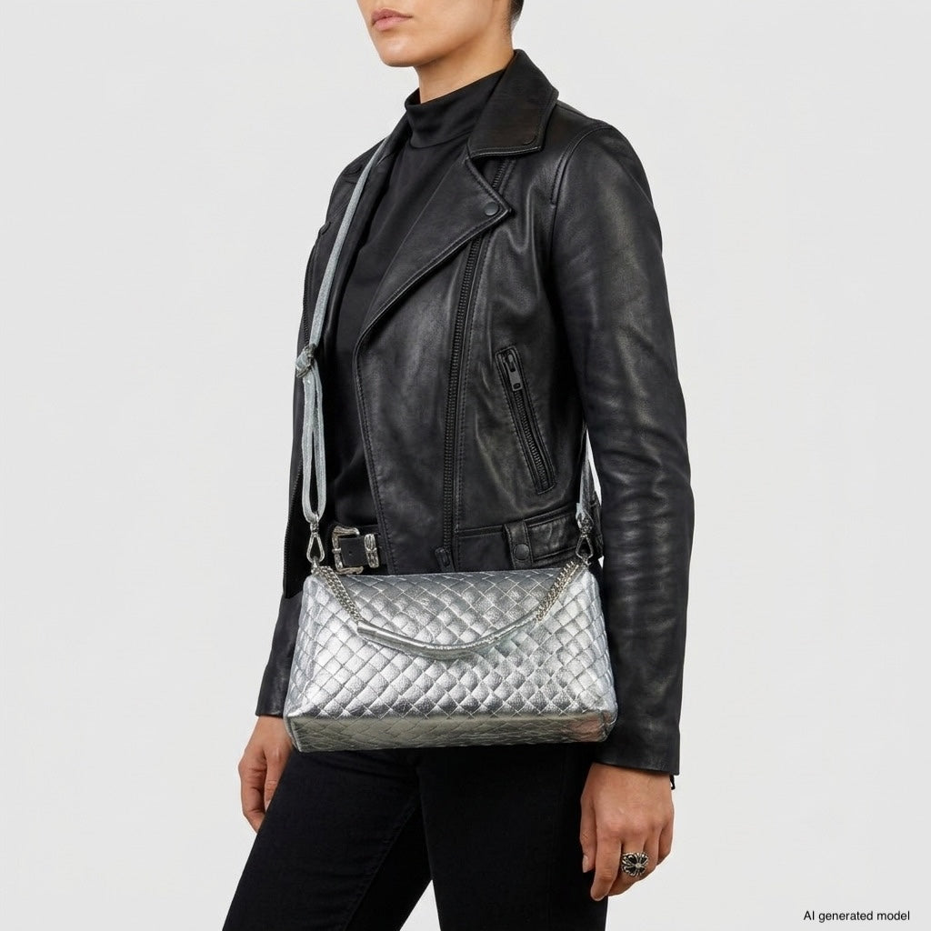 A person wearing a black leather jacket and black pants holds a luxury crossbody bag—a silver quilted handbag with a shoulder strap. The background is plain and white.