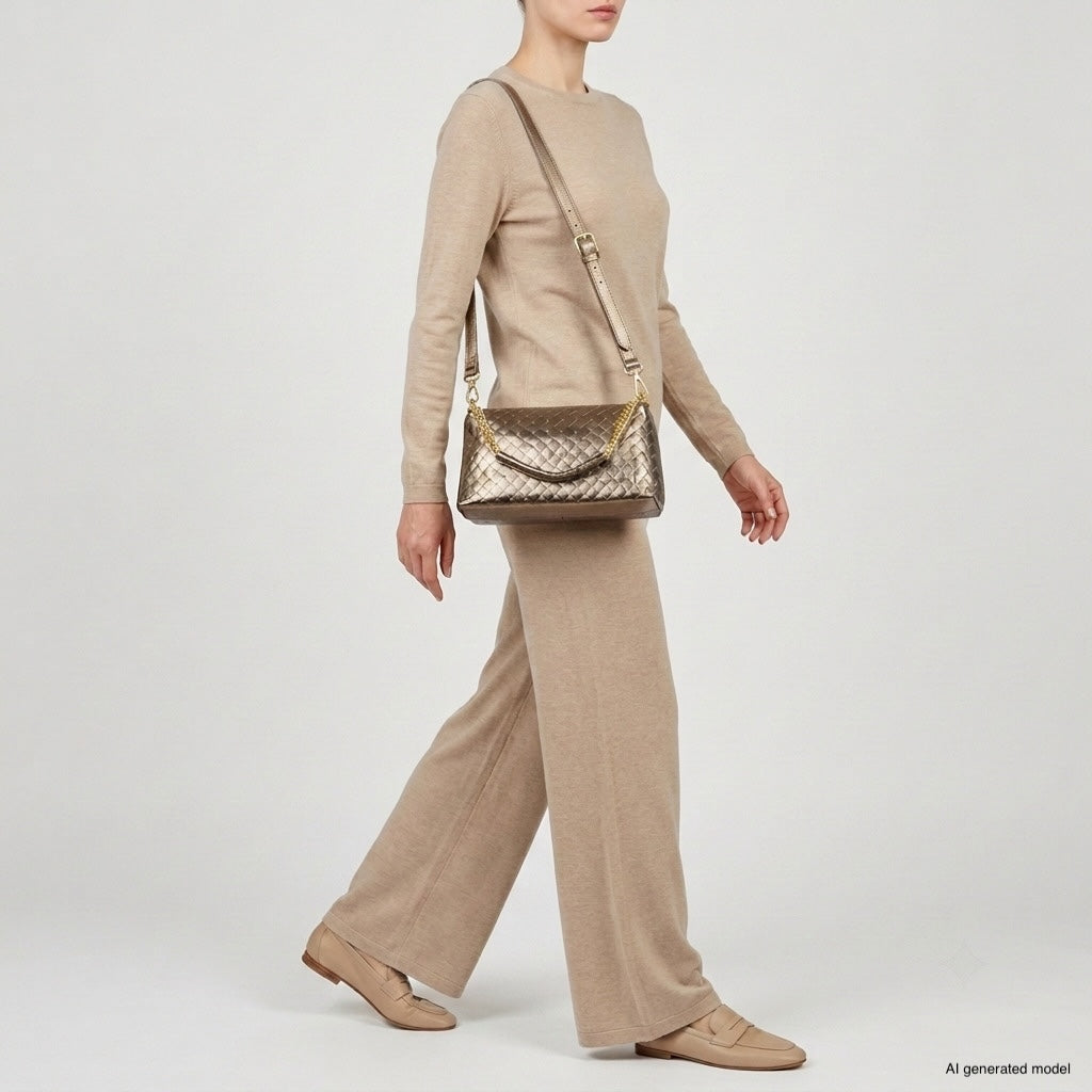 A person wearing a beige long-sleeve top and wide-leg pants walks while carrying a luxury crossbody bag over their shoulder. They also wear beige loafers. The background is plain and light-colored.