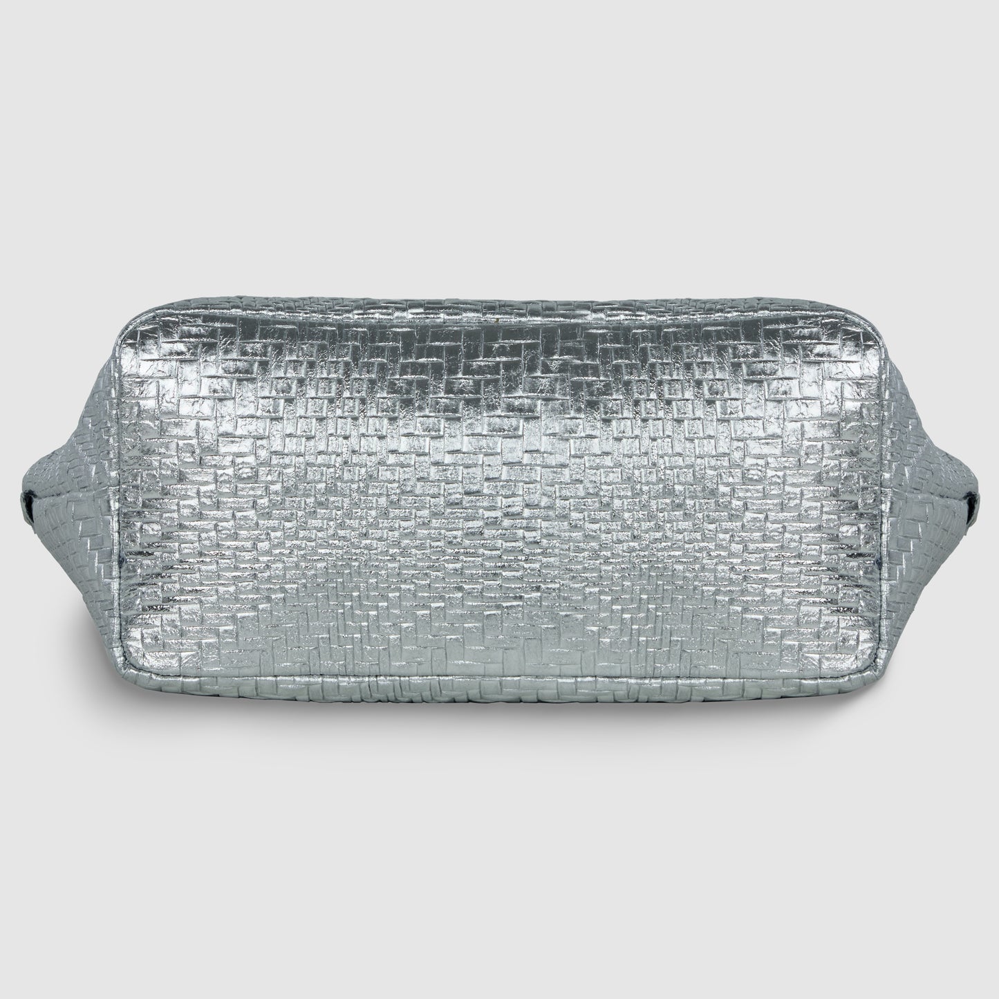 A rectangular, silver metallic suede bag with a textured, woven pattern and side handles, displayed against a plain light gray background.