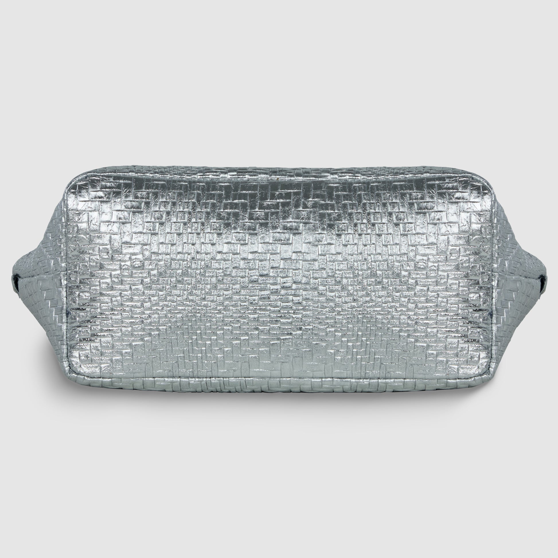 A rectangular, silver metallic suede bag with a textured, woven pattern and side handles, displayed against a plain light gray background.