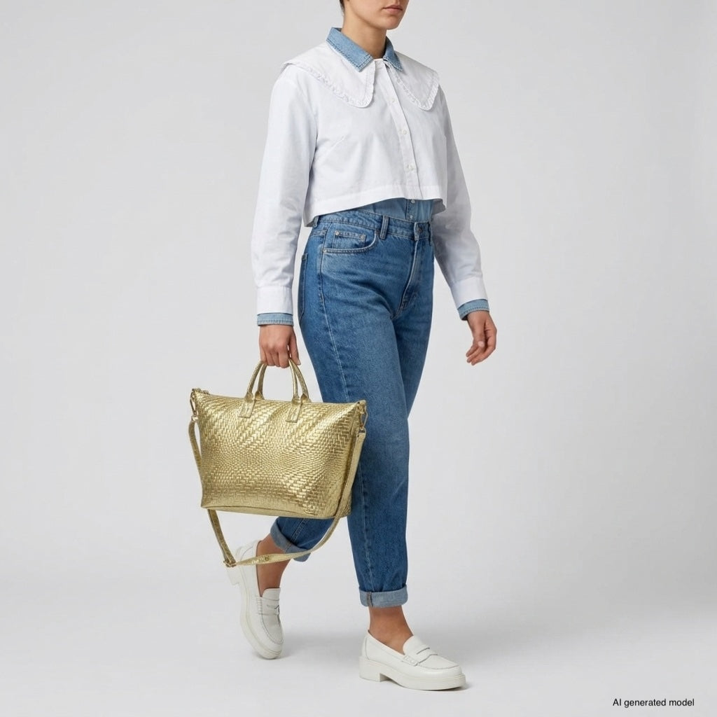 A person wearing a white collared shirt, blue high-waisted jeans, and white loafers walks while carrying an Italian suede handbag made in Italy. The background is plain light gray.