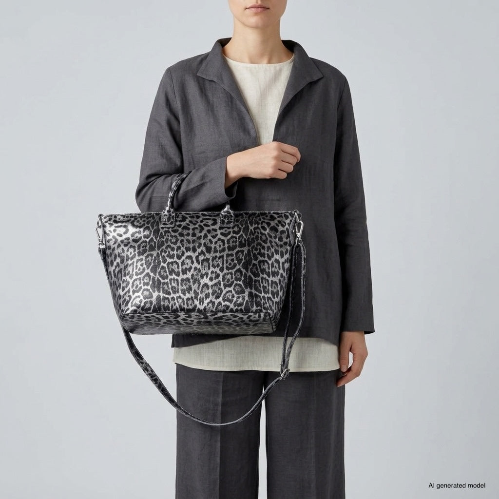 A person wearing a grey suit with a cream top holds an Italian leather handbag with a bold black-and-grey animal print and shoulder strap, standing against a plain light grey background.