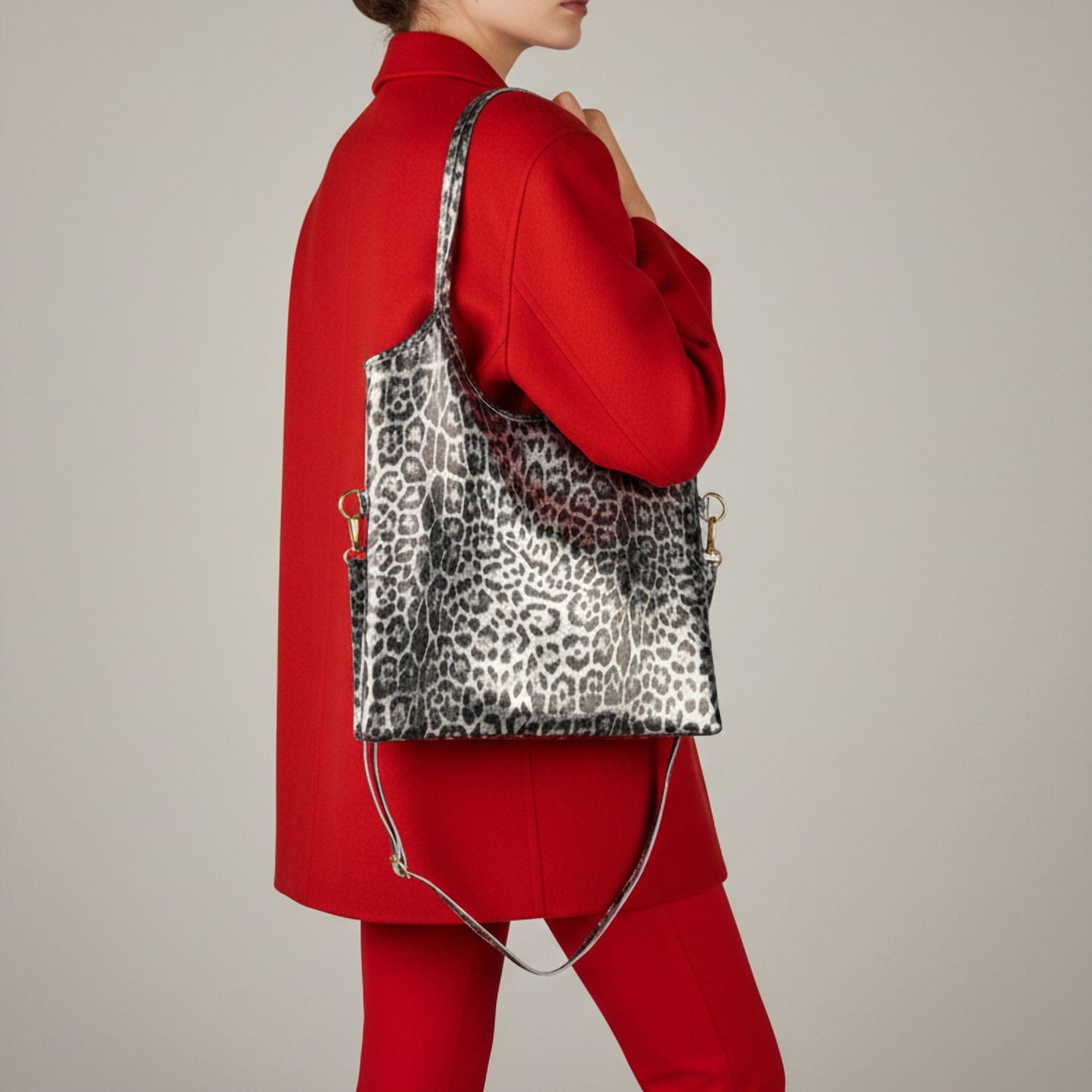 A person wearing a bright red blazer and pants holds a striking Italian handbag with black and white leopard print over one shoulder against a neutral background. The person’s face is not visible.