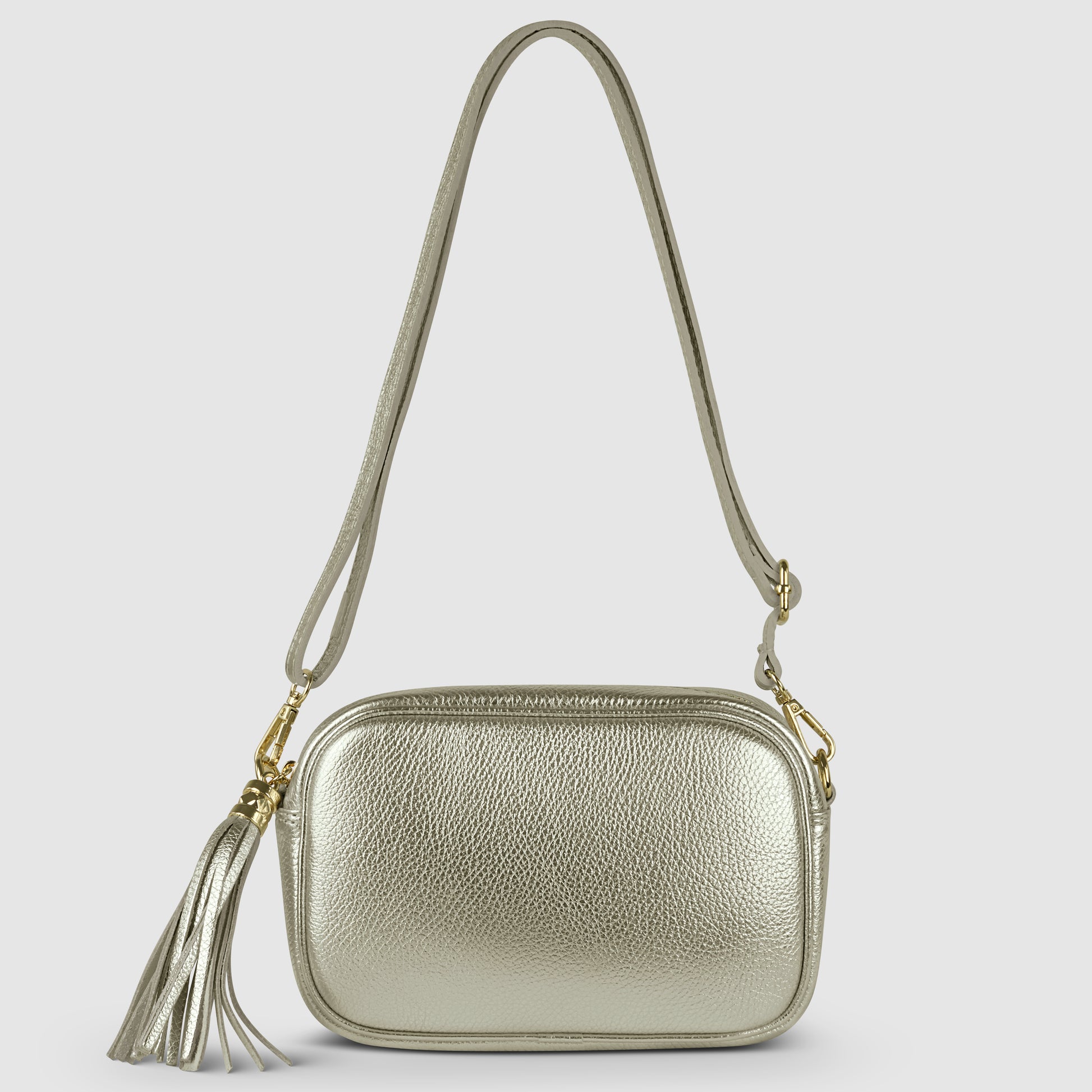 A small metallic silver crossbody handbag crafted from luster calfskin with a long strap, gold-tone hardware, and a decorative tassel on the side, set against a plain light gray background.
