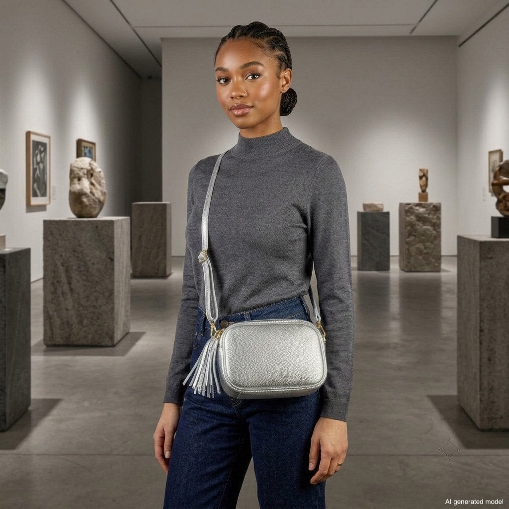 A woman in a grey sweater and jeans stands in an art gallery wearing a metallic finish purse, surrounded by sculptures and framed artwork on the walls.