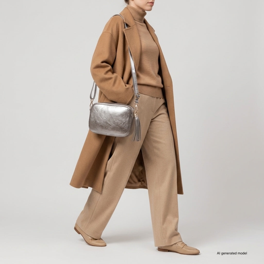 A person wearing a brown coat, tan turtleneck, and beige pants walks while carrying a compact rectangular handbag. The background is plain and light-colored.