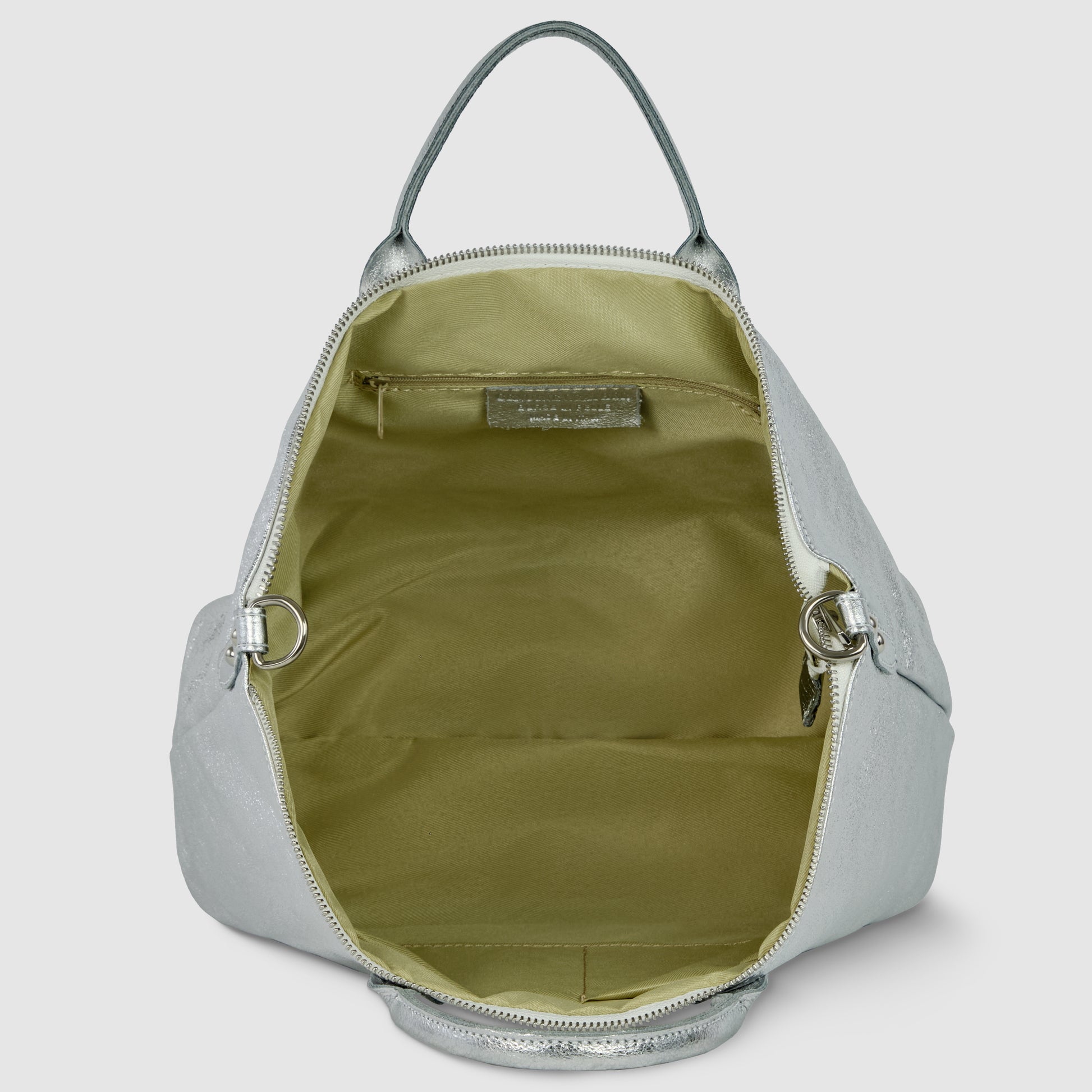 A silver geometric leather bag with its top zipper open reveals a spacious interior lined with light olive fabric and an inner pocket on the back wall. The bag features a handle on top and metal rings for straps.