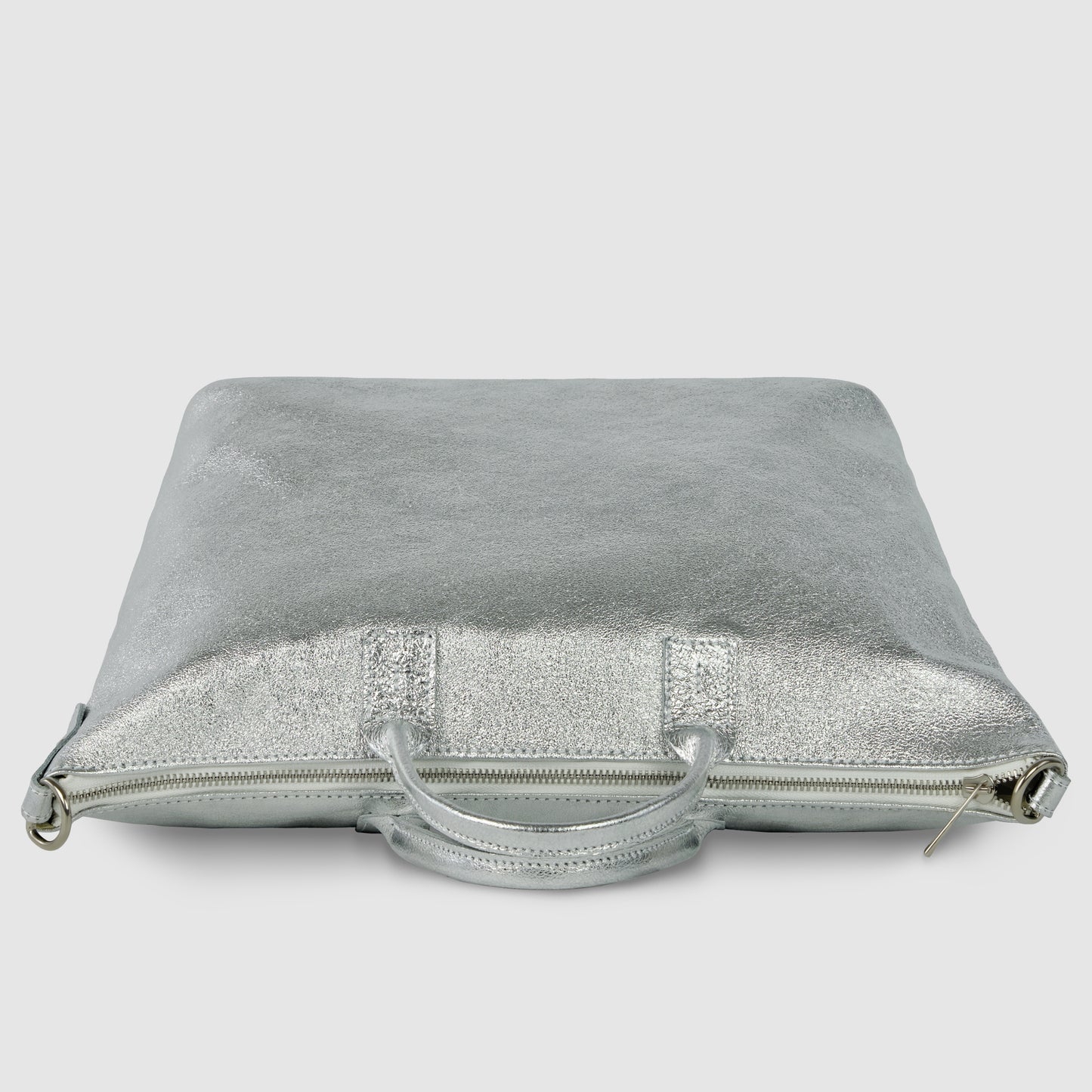 A square-shaped, metallic silver Italian handbag with a zipper and two handles lies flat against a plain, light gray background.