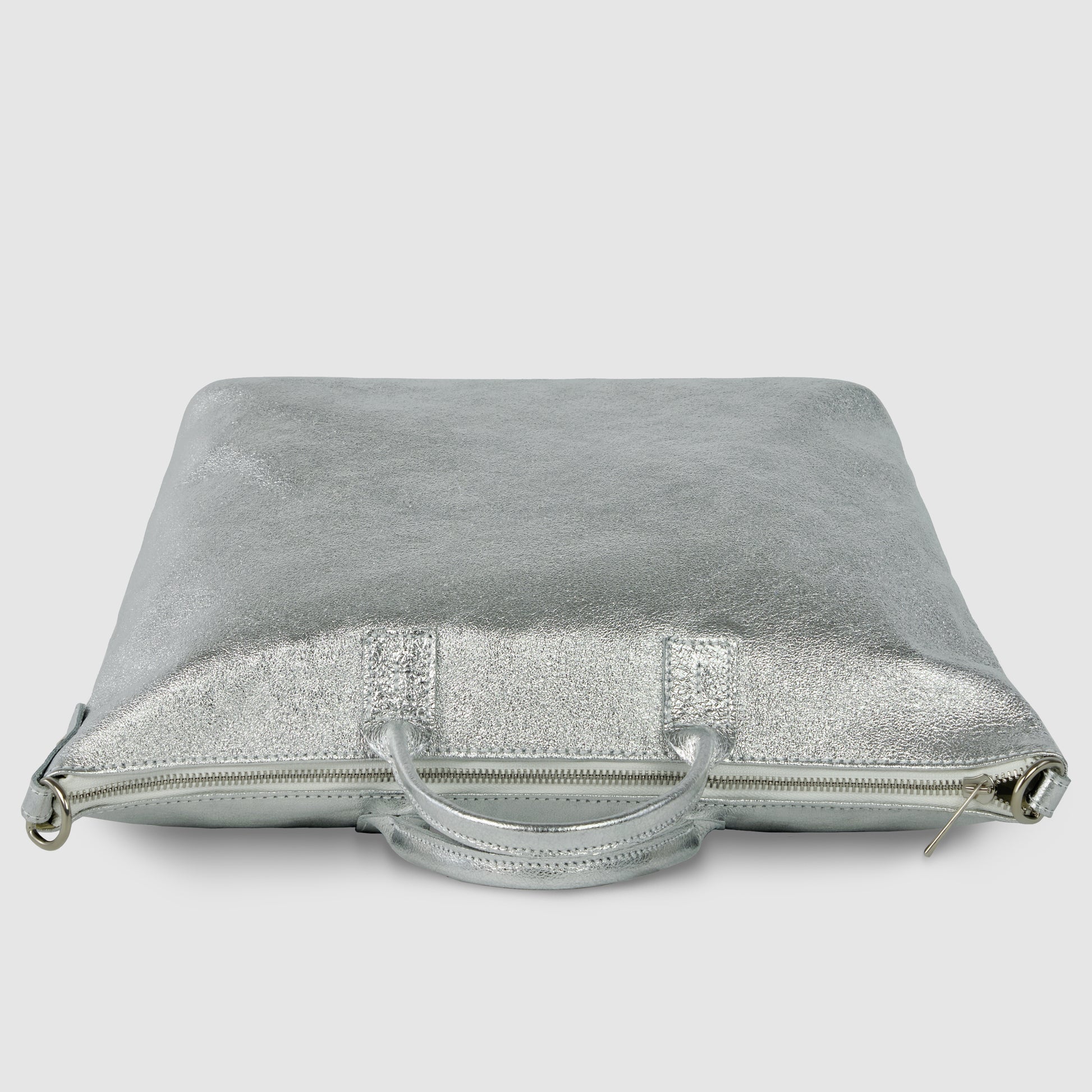 A square-shaped, metallic silver Italian handbag with a zipper and two handles lies flat against a plain, light gray background.