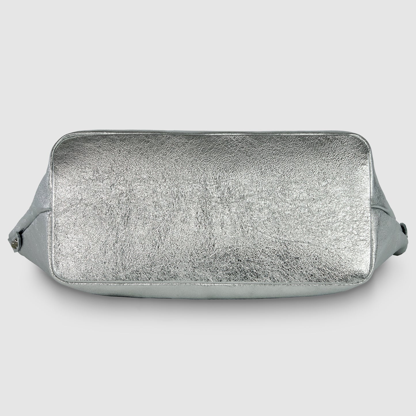 A rectangular geometric leather bag is shown from the bottom, featuring a textured, shiny silver surface and rounded edges, set against a plain light gray background.