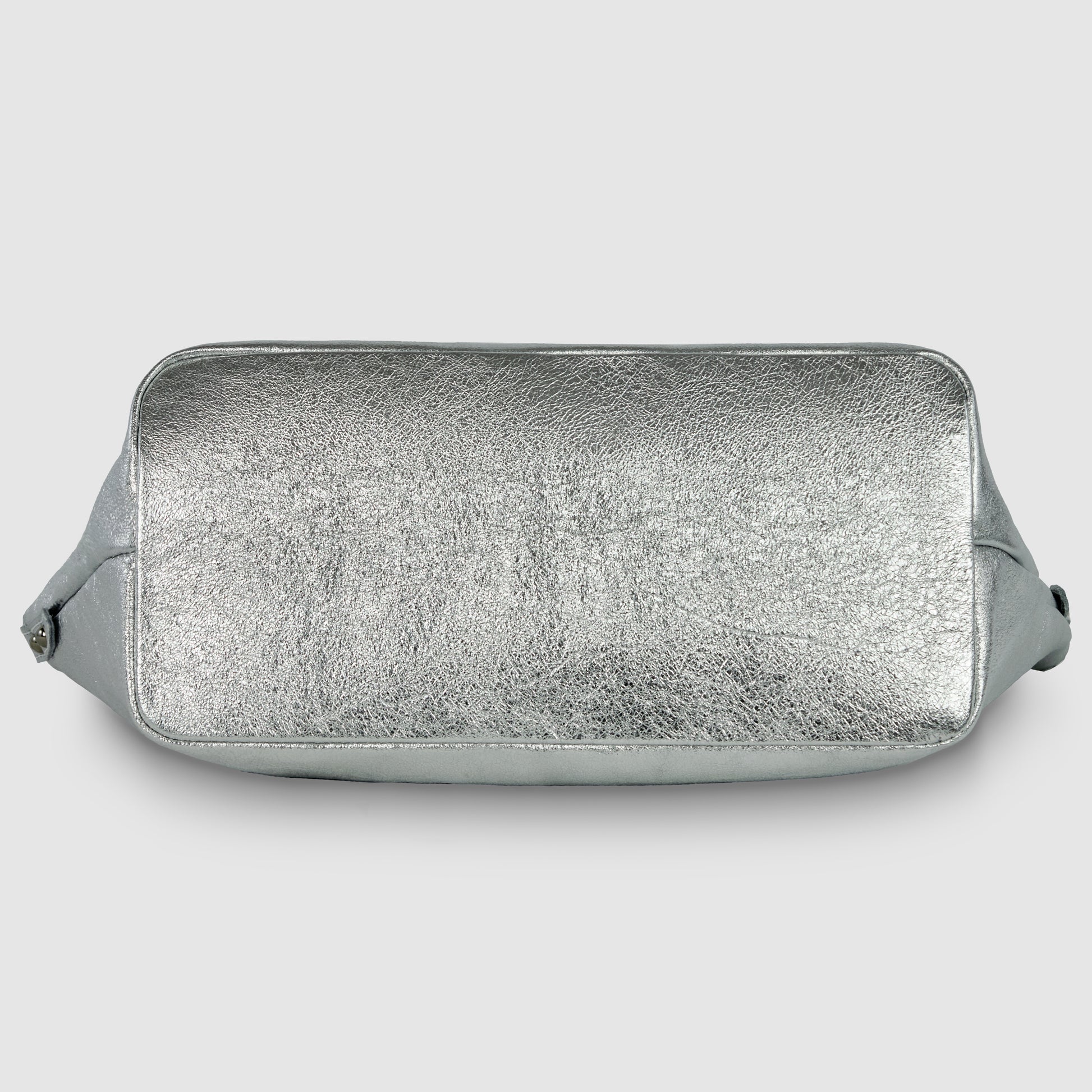 A rectangular geometric leather bag is shown from the bottom, featuring a textured, shiny silver surface and rounded edges, set against a plain light gray background.