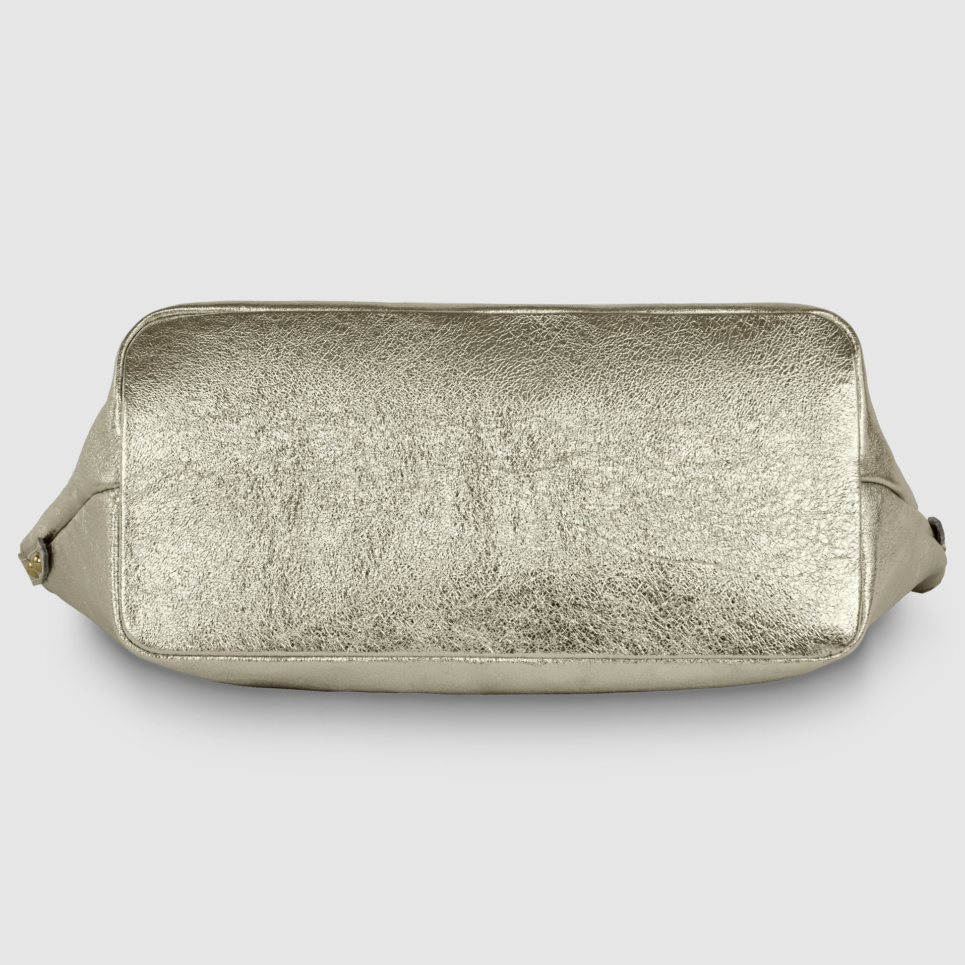 A metallic gold geometric leather bag lies flat on its back, displaying the textured bottom side against a plain light gray background.